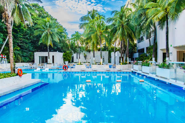 Alberca exterior con camastros y zona de relajación rodeada de palmeras en el Hotel Smart Cancun